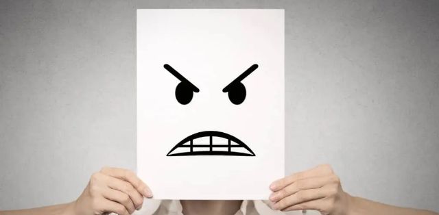 a person holding up a piece of paper with an angry cartoon face in front of them.