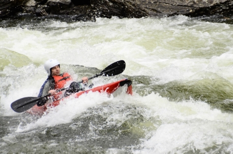 man in boat paddling rapids in a river.